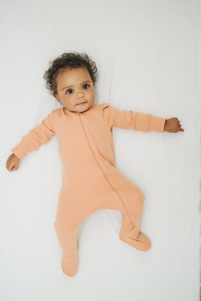 Baby wearing a peach-colored onesie on a white background